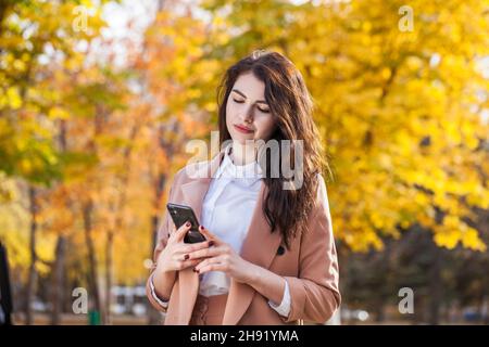 Young beautiful business woman making a cell phone call in autumn park Stock Photo