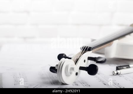 Close view of a violin and musical notes near white brick wall Stock Photo