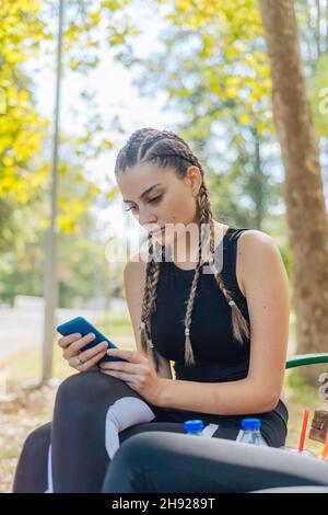 Hot attractive women smiling and swiping on their phones while sitting in a park and taking a break from their sports activities. Stock Photo