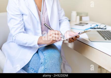 Anonymous doctor writing on clipboard. Filling patient form. Doing paperwork in medical clinic Stock Photo