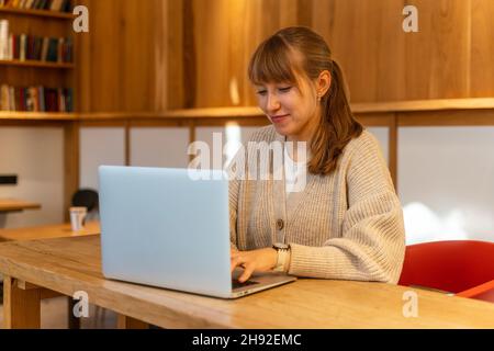 Young happy female using laptop in cafe. Remote work far from home. Horizontal Stock Photo