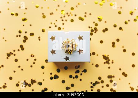 Gift white box with a gold tape with tinsel and confetti on a white background. The concept of a gift, a new year, a festive background. Flat lay, top view. Stock Photo