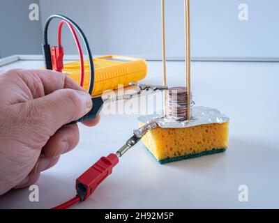 Measuring electric voltage on Volta's pile made from a stack of copper coins, filter paper in salt water and aluminum foil. Stock Photo