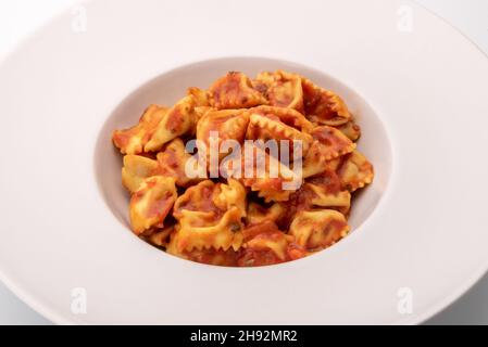 Typical agnolotti del plin, stuffed egg pasta ravioli from Langhe, Piedmont, Italy, seasoned with tomato sauce in white dish Stock Photo