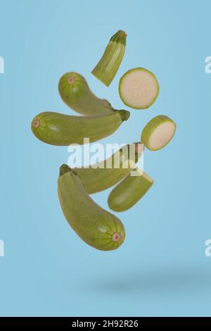 Fresh organic zucchini, whole and sliced flying freely in the air against blue background. Creative concept of fresh vegetables, diet, flying food. Stock Photo