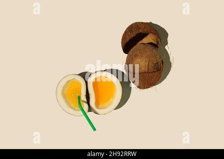 Top view of cut coconuts with orange juice and a straw isolated on a beige background Stock Photo