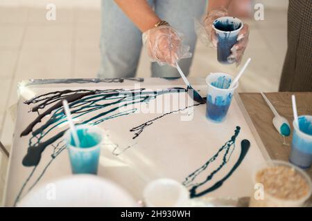 Epoxy resin different blue color in cup for abstract art. Woman hands process of making accessory from resin.Mixing colorful of resin chemical in Stock Photo