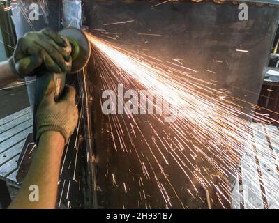 caucasian hands using an angle grinder on metal barrel vessel close-up with long sparks trails Stock Photo