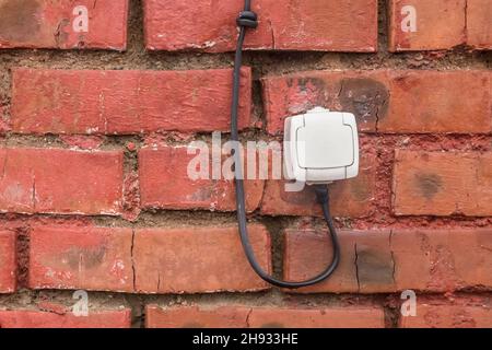 Old white socket on a reddish-brown brick wall background. Stock Photo