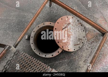 Old dirty fuel open hatch for cleaning from liquid chemical waste and oil of an abandoned tank industrial plant. Stock Photo