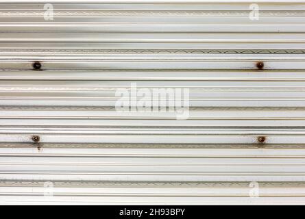 detail image of a textured aluminum panel with four rusted screws Stock Photo