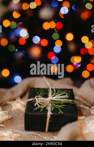 small gift laying on beige textile, decorated Christmas tree on background. Stock Photo