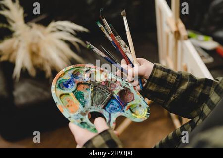 Close up on hands of unknown female artist painter holding color palette and paintbrush brushes ready to make art leisure activity professional or ama Stock Photo