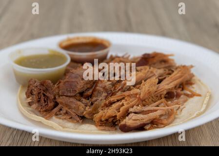 Generous portion of carnitas pork meat on a tortilla with red and green salsa for this taco meal. Stock Photo