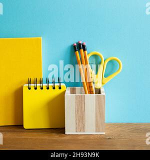 Yellow notebook, pencil holder, scissor, ruler on wooden desk. blue wall background. workspace Stock Photo