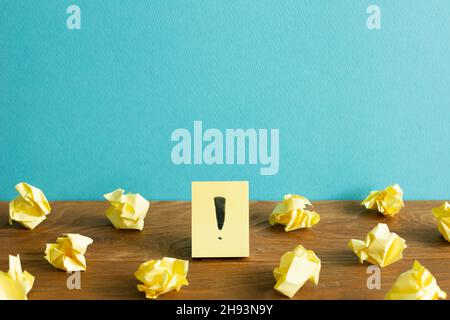 Crumpled paper balls and notepad with exclamation mark on wooden desk. blue wall background. Thinking, solution, business, idea concept Stock Photo