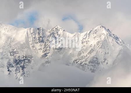 Snowy covered mountain top on winter with misty, cloud covered snow, high altitude peak. Landscape, stunning nature background. Stock Photo