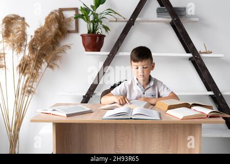 Back to school. Schoolboy boy reading books at the table in the library or home school. Pupil in class at a table with textbooks. Child student doing Stock Photo