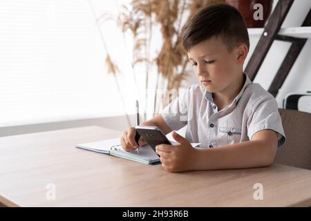 digital generation child doing homework using a mobile phone. Lessons with a gadget via the Internet. A schoolboy writes tests from a smartphone Stock Photo