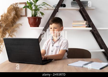 child working at laptop online education remote tutor. concentrated schoolboy doing homework by typing text on the keyboard. Watching a teaching video Stock Photo