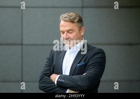 Stylish confident middle-aged man with closed eyes standing with folded arms looking down Stock Photo