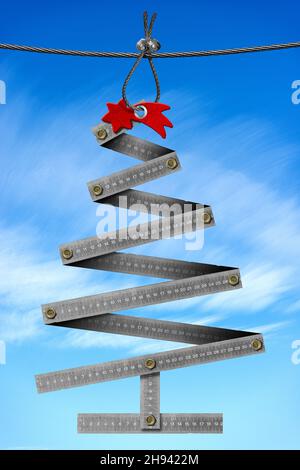 Metal folding ruler in the shape of a Christmas tree and a red comet star hanging from a steel cable against a blue sky and clouds on background. Stock Photo