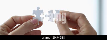 Female hands holding two white puzzle pieces closeup Stock Photo