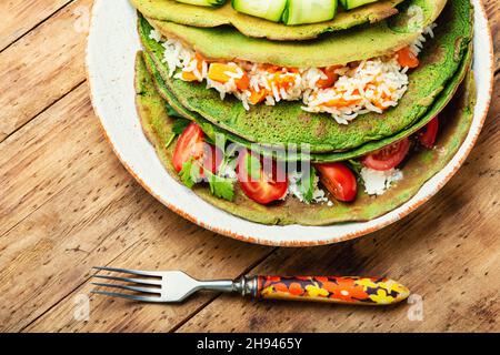 Green spinach pancakes stuffed with rice and vegetables on rustic wooden table Stock Photo