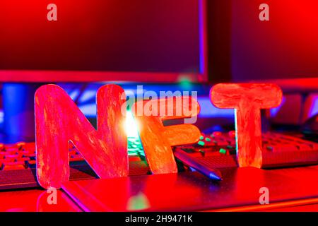 NFT ( Non-Fungible Token ) text of letters illuminated with neon light. Workplace of a graphic designer creating NFT digital art. Concept of cryptoart Stock Photo