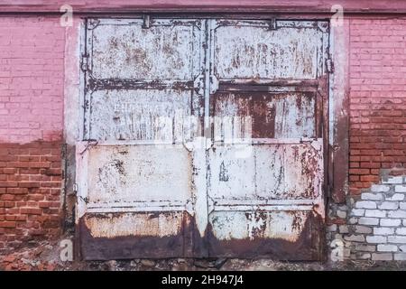 Old dirty worn weathered iron warehouse door with brick wall of building abandoned architecture. Stock Photo