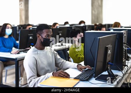 Young multiracial students taking an exam in high school while wearing face mask during corona virus pandemic - Education and technology concept Stock Photo