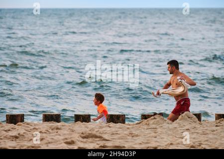 Svetlogorsk, Russia - 07.31.2021 - Father and little kid playing tag on sea beach, Baltic Sea background. Loving father and his son playing on beach. Stock Photo