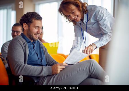 An elderly female lecturer is giving assistance to participants in a relaxed atmosphere during a business lecture. Business, people, meeting, company Stock Photo