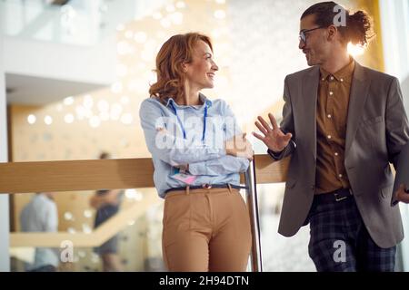 A female business manager is standing in the hallway and chatting in a pleasant atmosphere with her young male colleague. Business, people, company Stock Photo