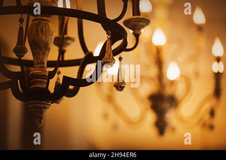 On the old and elegant chandeliers, lamps in the form of candles glow in the evening twilight. Decorative luxury lighting of the room. A palace or a h Stock Photo