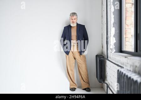 Full length shot of stylish middle aged man in business casual wear looking at camera, putting hands in pockets while posing against white background Stock Photo