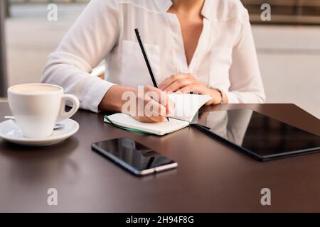 unrecognizable businesswoman working and taking notes on the terrace of a coffee shop, concept of digital entrepreneur and urban lifestyle Stock Photo