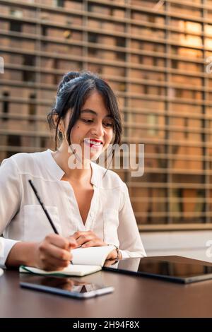 businesswoman working and taking notes on the terrace of a coffee shop, concept of digital entrepreneur and urban lifestyle, copy space for text Stock Photo