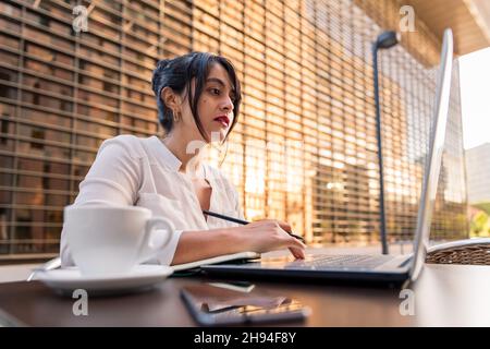 businesswoman working with her computer on the terrace of a coffee shop in the financial district, concept of digital entrepreneur and urban lifestyle Stock Photo