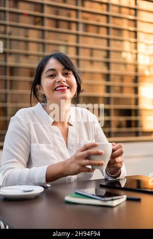 smiling businesswoman working and drinking coffee on the terrace of a coffee shop, concept of digital entrepreneur and urban lifestyle, copy space for Stock Photo