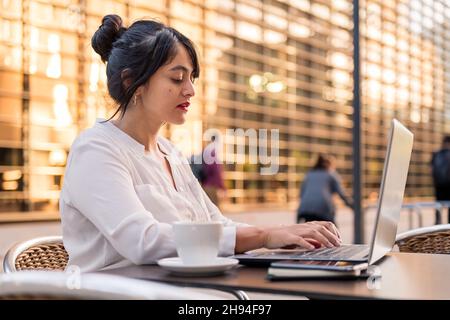 businesswoman typing on her laptop on the terrace of a coffee shop in town, concept of digital entrepreneur and urban lifestyle, copy space for text Stock Photo