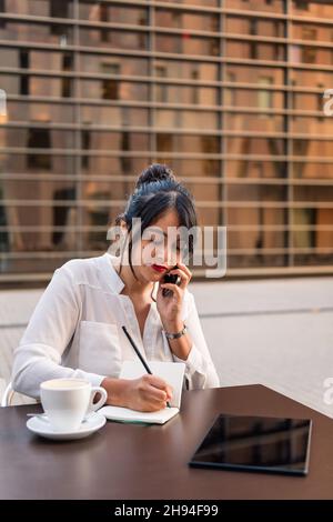 businesswoman working and talking on the phone on the terrace of a coffee shop, concept of digital entrepreneur and urban lifestyle, copy space for te Stock Photo