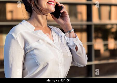 unrecognizable businesswoman smiling on the phone in front of an office building, concept of successful entrepreneur and urban lifestyle, copy space f Stock Photo