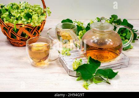 Teapot and two cups of tea with a linden tree on a wooden table. Healing tea. Stock Photo