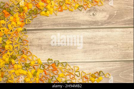 Frame of multicolored pasta in the shape of a heart on a wooden background, top view, copy space, selective focus Stock Photo