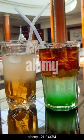 Two multicolored cocktails with different fillings with straws in glass glasses Stock Photo