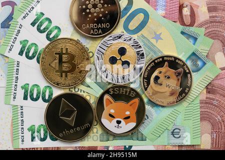 Bitcoin, Cardano, Shiba Inu, Ethereum, Ripple, and Dogecoin physical coins laying on top of 100 and 10 Euro bills. Stock Photo