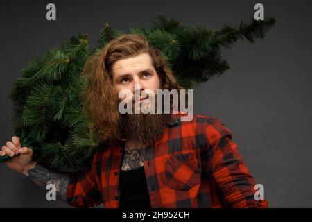 handsome man with long hair holding a synthetic christmas tree. Stock Photo