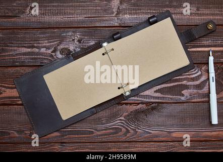 notebook with craft paper in an unfolded form lies on a wooden surface with a white fountain pen Stock Photo