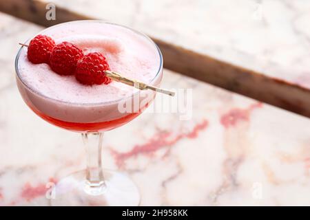 Clover Club Cocktail Drink with Egg White Foam and Raspberry Garnish in Coupe Glass on Marble Windowsill Stock Photo